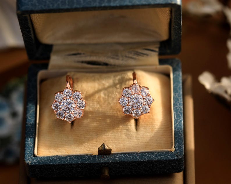Puede incluir: Un par de pendientes de oro rosa con un racimo de piedras de circonita c&uacute;bica transparentes en forma de flor. Los pendientes est&aacute;n en una peque&ntilde;a caja de terciopelo.