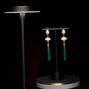 May include: A pair of green gemstone dangle earrings with a gold setting and a fan-shaped design with clear rhinestones.