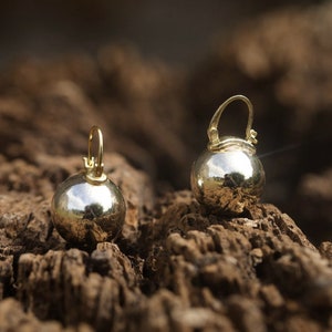 K&ouml;nnte beinhalten: Ein Paar goldene Kugelohrringe mit einer glatten, reflektierenden Oberfl&auml;che. Die Ohrringe h&auml;ngen an einem kleinen Ring.