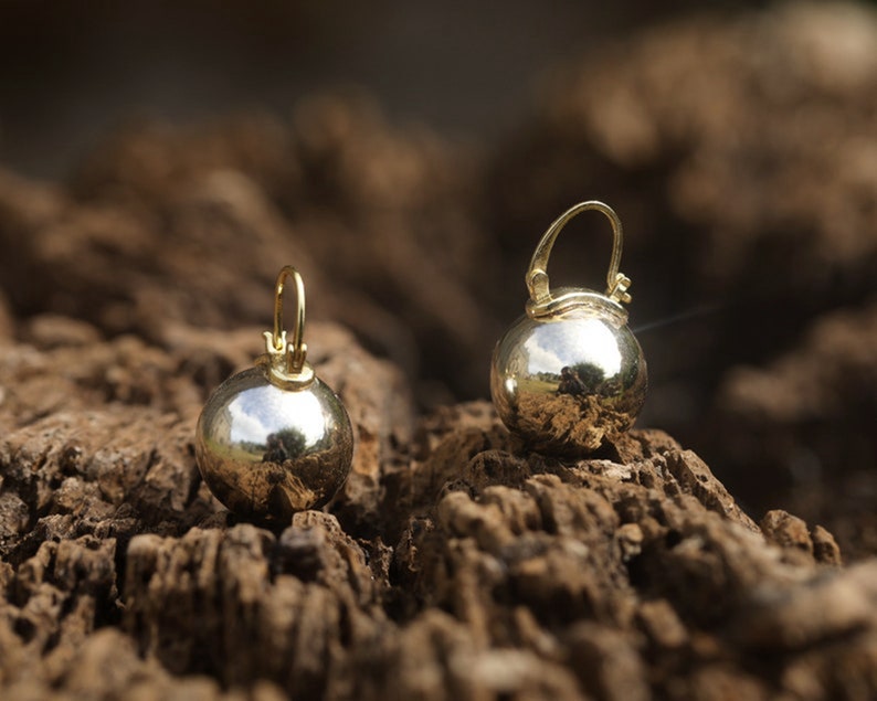 K&ouml;nnte beinhalten: Ein Paar goldene Kugelohrringe mit einer glatten, reflektierenden Oberfl&auml;che. Die Ohrringe h&auml;ngen an einem kleinen Ring.