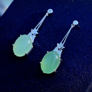 May include: A pair of silver earrings with green gemstone drops and small clear stones. The earrings have a delicate, art deco design.