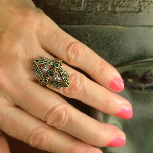 Pode incluir: Um anel de ouro com um design de lib&eacute;lula. A lib&eacute;lula tem asas de esmalte verde e strass transparentes e verdes.