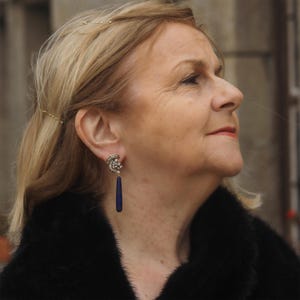 Könnte beinhalten: Eine Frau trägt einen schwarzen Pelzmantel mit langen, baumelnden Ohrringen. Die Ohrringe sind silberfarben mit einem Cluster aus klaren Steinen und einem langen, dunkelblauen Tropfenanhänger.