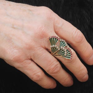 Può includere: Un anello d'oro con un designo in smalto verde e rosso. L'anello presenta un designo a forma di ventaglio con pietre bianche.