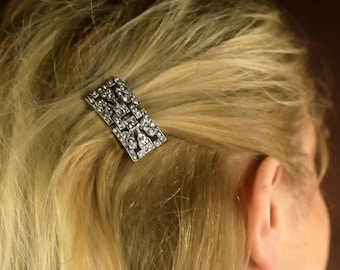 May include: A silver hair clip with a geometric design and clear rhinestones.