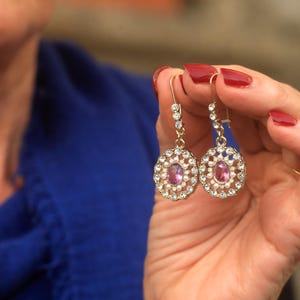 May include: A pair of gold earrings with a pink oval gemstone surrounded by white pearls.