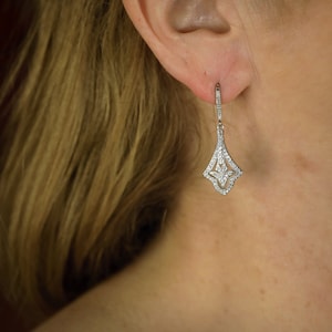 May include: Silver dangle earrings with a teardrop-shaped design featuring a geometric pattern of small clear stones.