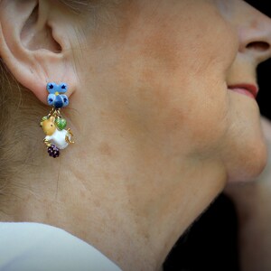 May include: A pair of dangle earrings with a blue butterfly charm, a white and brown animal charm, and green and purple beads.