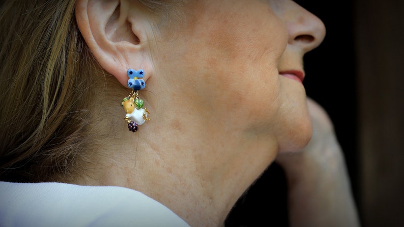 May include: A pair of dangle earrings with a blue butterfly charm, a white and brown animal charm, and green and purple beads.
