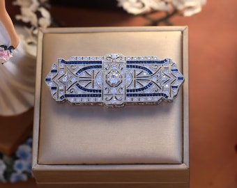 May include: A silver and blue Art Deco style brooch with a geometric design and a large central stone.