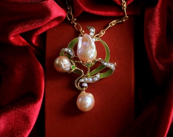 May include: A gold-tone necklace featuring a pendant shaped like a tulip flower. The pendant is adorned with three large, iridescent peach-colored pearls, small white seed pearls, and green enamel accents. The chain consists of oval links.