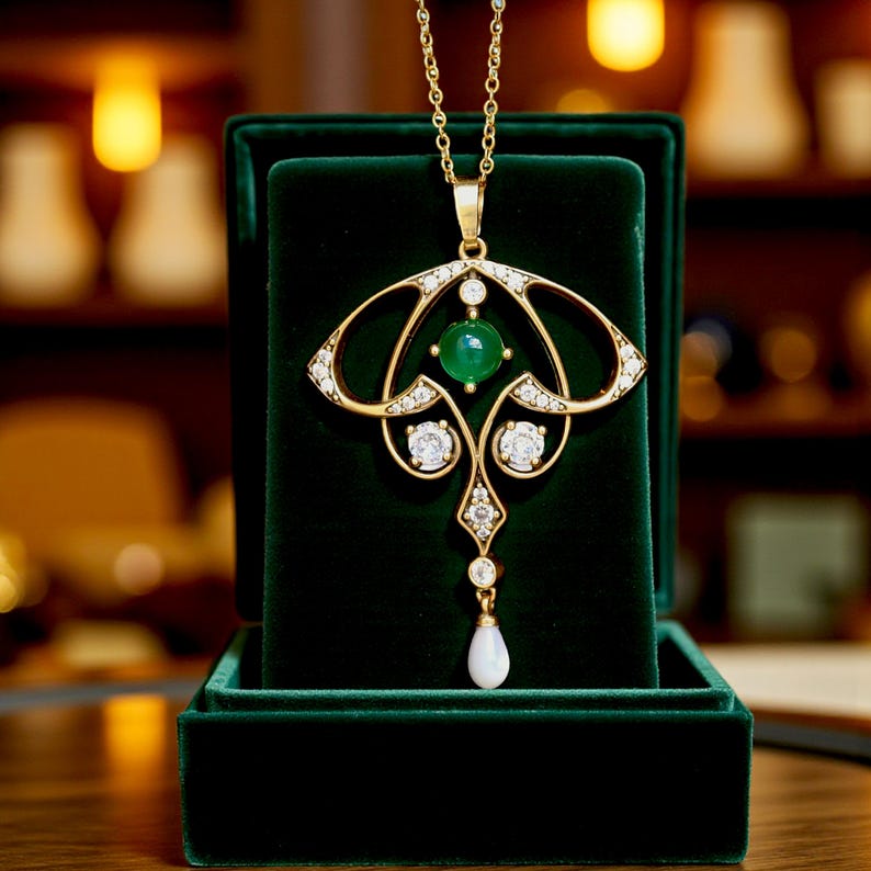 May include: A gold-colored pendant necklace with an Art Nouveau design, featuring a central green gemstone, clear accent stones, and a pear-shaped drop. The necklace is displayed in a dark green velvet jewelry box.