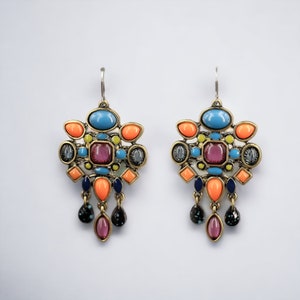 Pode incluir: Um par de brincos pendurados com um design geométrico. Os brincos são feitos de metal dourado e apresentam uma variedade de pedras coloridas, incluindo turquesa, rosa, laranja e amarelo.