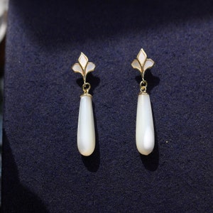 May include: A pair of white teardrop-shaped earrings with gold accents and a floral design.
