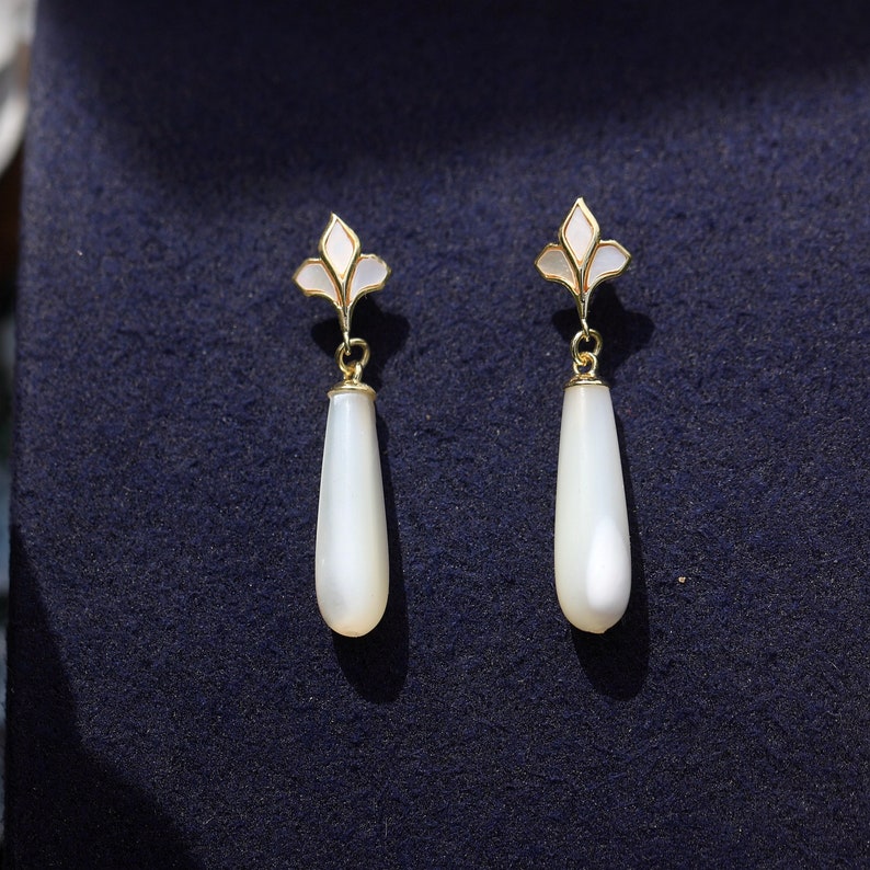 May include: A pair of white teardrop-shaped earrings with gold accents and a floral design.
