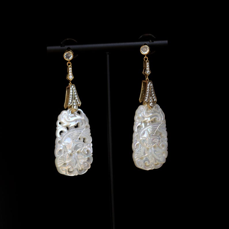 May include: A pair of gold earrings with white mother of pearl carved pendants and clear crystal accents.
