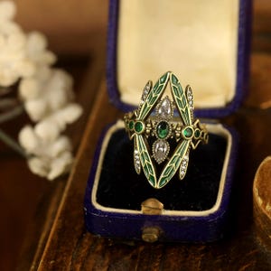 Pode incluir: Um anel de ouro com um design de lib&eacute;lula. As asas da lib&eacute;lula s&atilde;o de esmalte verde com detalhes brancos. O anel tem tr&ecirc;s pedras preciosas em forma de p&ecirc;ra, duas verdes e uma transparente.