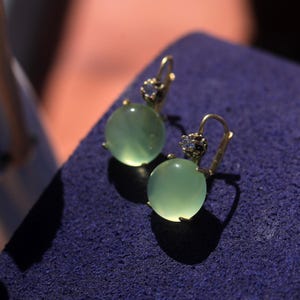 May include: A pair of green gemstone earrings with gold settings and small diamond accents.