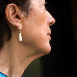 May include: A woman with short dark hair wearing a single pearl drop earring.
