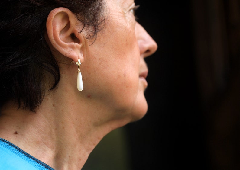 May include: A woman with short dark hair wearing a single pearl drop earring.