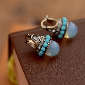 May include: A pair of dangle earrings with a light blue stone and turquoise beads. The earrings have a gold tone finish.