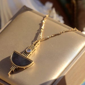 Pode incluir: Um colar de ouro com um pingente geom&eacute;trico que apresenta uma forma de meia lua em preto e branco e um strass transparente. O pingente &eacute; de estilo art d&eacute;co moderno.