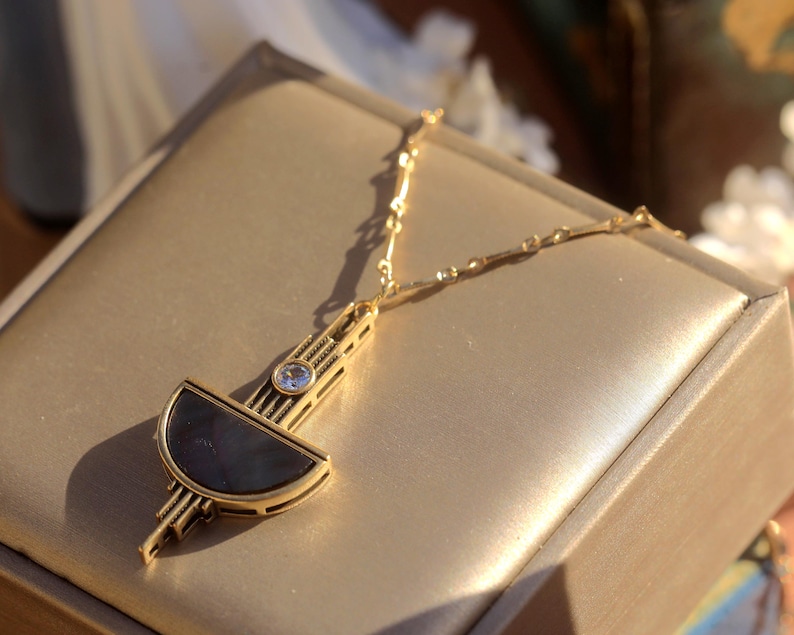 Pode incluir: Um colar de ouro com um pingente geom&eacute;trico que apresenta uma forma de meia lua em preto e branco e um strass transparente. O pingente &eacute; de estilo art d&eacute;co moderno.