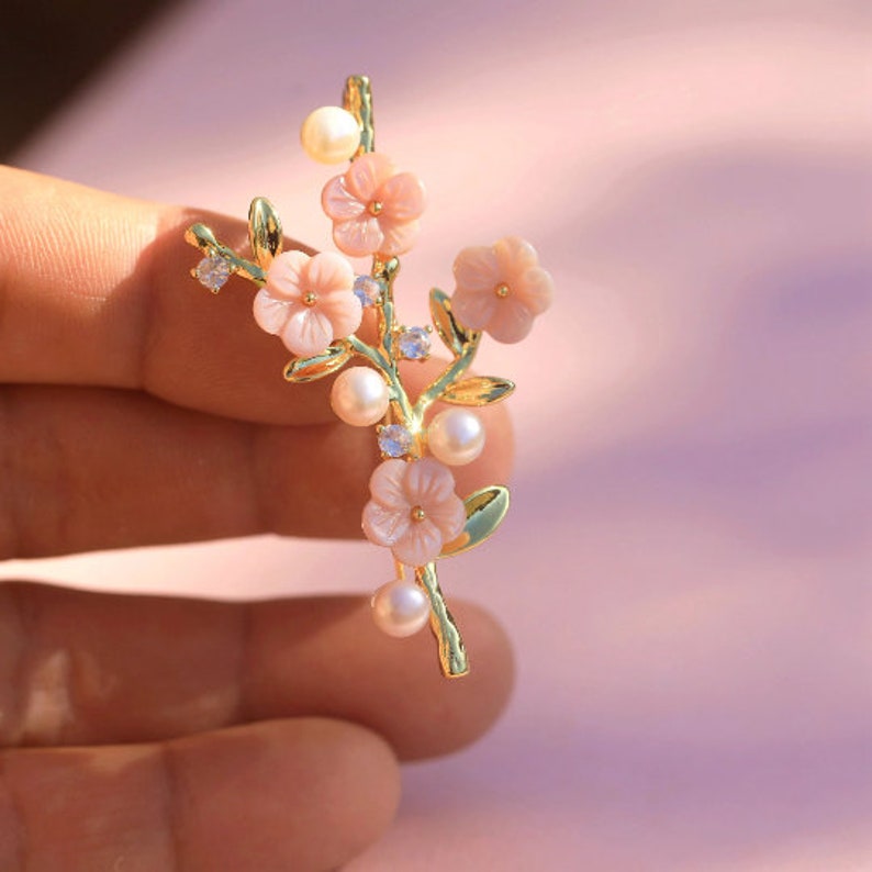 May include: A gold-tone brooch featuring a delicate floral design with pink flowers and pearl accents.