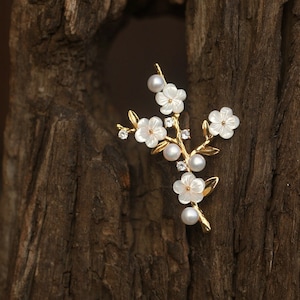 May include: A gold-tone brooch with a delicate branch design featuring white pearl-like flowers and small clear rhinestones.