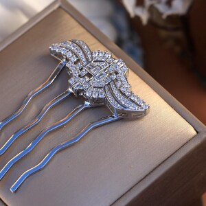 May include: A silver hair comb with a decorative design featuring a large, clear crystal in the center surrounded by smaller crystals. The comb has four tines.