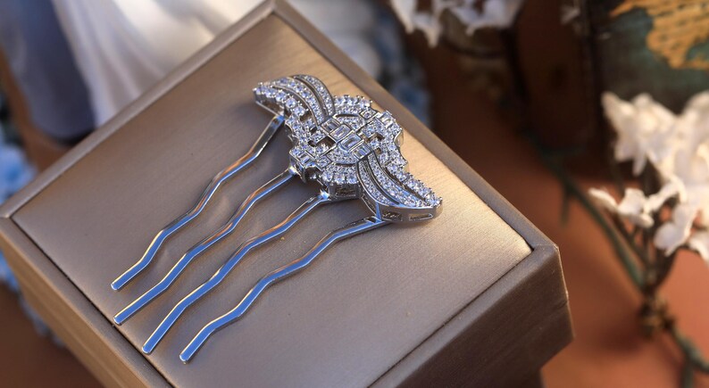 May include: A silver hair comb with a decorative design featuring a large, clear crystal in the center surrounded by smaller crystals. The comb has four tines.