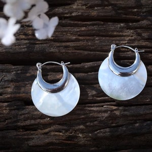 May include: A pair of silver hoop earrings with a white mother-of-pearl inlay. The earrings are round and have a crescent moon shape.