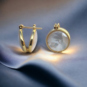 May include: A pair of gold hoop earrings with a white mother-of-pearl inlay. The earrings are round and have a smooth, polished finish.