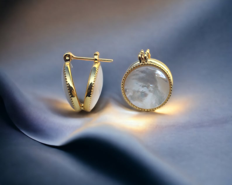 May include: A pair of gold hoop earrings with a white mother-of-pearl inlay. The earrings are round and have a smooth, polished finish.