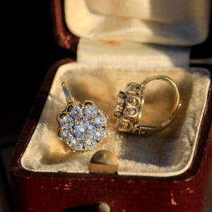 Puede incluir: Un par de pendientes de oro con un dise&ntilde;o en forma de flor engastado con piedras preciosas transparentes. Los pendientes est&aacute;n en una caja de joyer&iacute;a forrada de terciopelo.