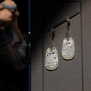 May include: A pair of white, intricately carved earrings with gold accents and clear stones. The earrings are oval shaped and feature a floral design.