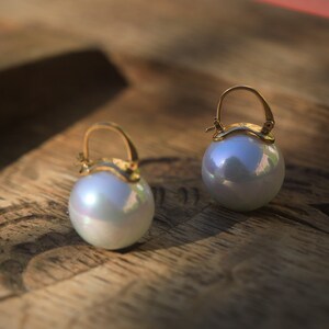 May include: A pair of gold hoop earrings with large, iridescent white pearl drops.