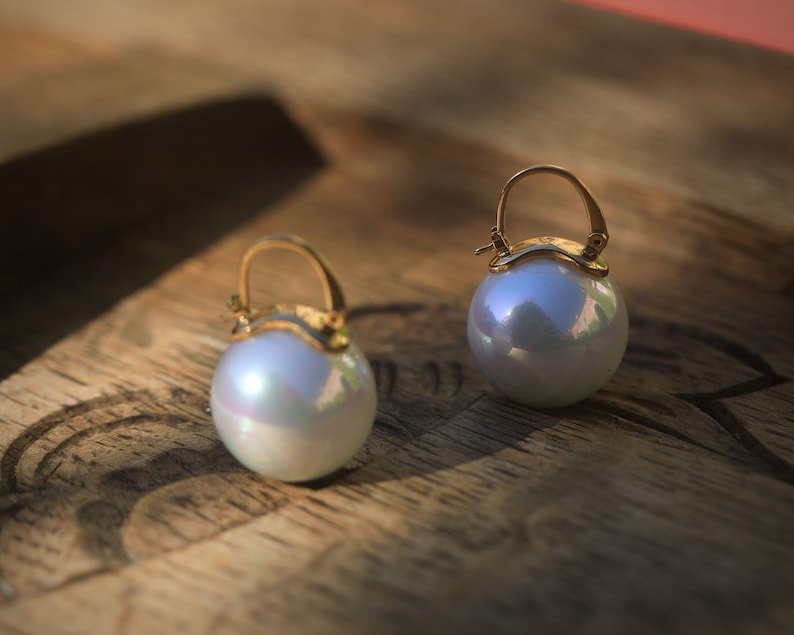 May include: A pair of gold hoop earrings with large, iridescent white pearl drops.