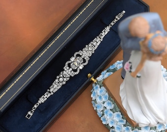 May include: A silver bracelet with a floral design and clear rhinestones. The bracelet is displayed in a blue velvet box with a brown wooden exterior.