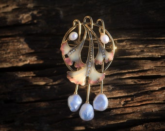 May include: A gold-tone brooch with a delicate design of three ginkgo leaves, each with a pink and white enamel finish. The leaves are accented with small clear rhinestones and three pearl-like drops hang from the bottom.