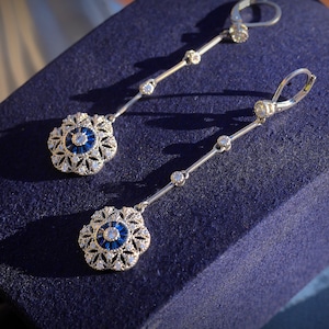 May include: A pair of silver dangle earrings with blue and white stones. The earrings feature a delicate floral design.