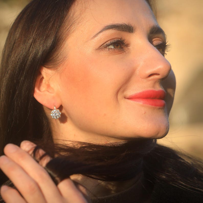 Puede incluir: Una mujer con el pelo largo y oscuro que lleva un pendiente de aro plateado con un racimo de peque&ntilde;as piedras blancas.