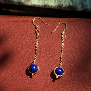 May include: A pair of gold dangle earrings with blue gemstone drops. The earrings feature a delicate chain and a round blue stone.