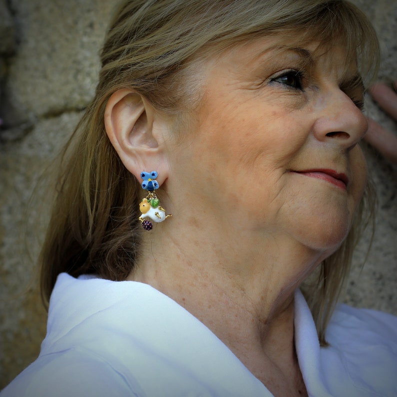 May include: A pair of dangle earrings with a blue flower charm, a white and yellow bird charm, and a purple berry charm.