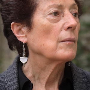 May include: A silver-toned drop earring featuring a vertical rectangular bar with a small circular clear stone at the top and a semi-circular white inlay at the bottom, suspended from a simple silver-toned hook wire for pierced ears.