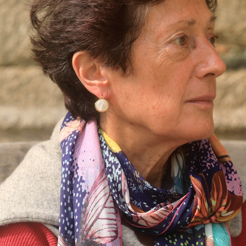 May include: A woman wearing a colorful patterned scarf with a white pearl earring. The earring has a gold setting.