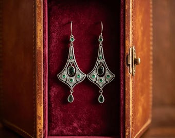 May include: A pair of silver-toned drop earrings featuring intricate filigree metalwork, each set with multiple small round green stones and a single larger oval green stone in the center, finished with a dangling teardrop-shaped green stone.