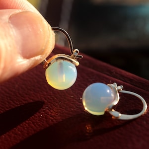 Könnte beinhalten: Ein Paar goldene Creolen mit Opal-Steinen. Die Steine sind hellblau und weiß.