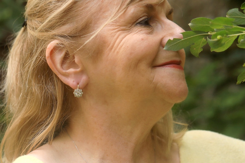 Puede incluir: Primer plano de la cara de una mujer, ella est&aacute; sonriendo y mirando hacia la derecha. Lleva un peque&ntilde;o pendiente de plata en forma de flor en la oreja izquierda. Su cabello es rubio y est&aacute; recogido hacia atr&aacute;s de su cara.
