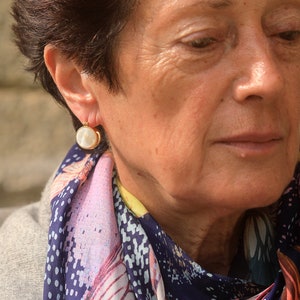 May include: A woman wearing a gold earring with a white pearl-like stone. The earring is a simple design with a small gold hoop.